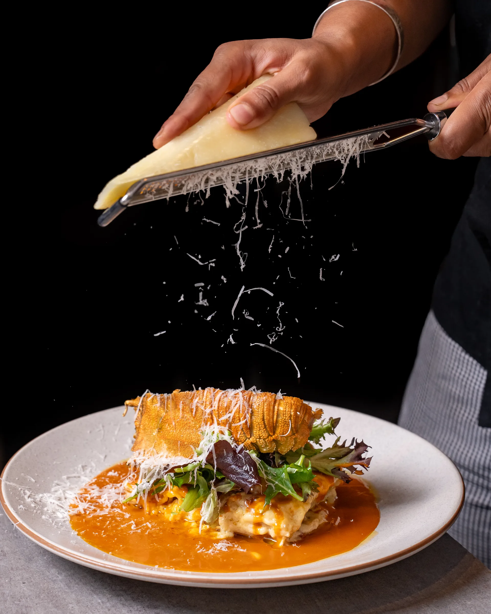 Chef grating Pecorino over sand crab lasagna — Sage Yellowfin